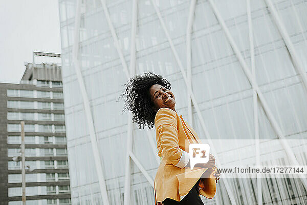 Lächelnde Unternehmerin mit geschlossenen Augen vor einem Bürogebäude stehend