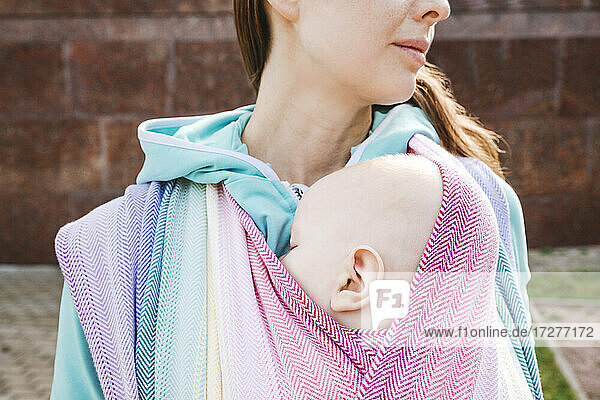 Midsection Mutter trägt Baby in Decke eingewickelt stehend auf sonnigen Tag