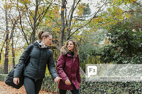Smiling beautiful female friends walking at park during autumn