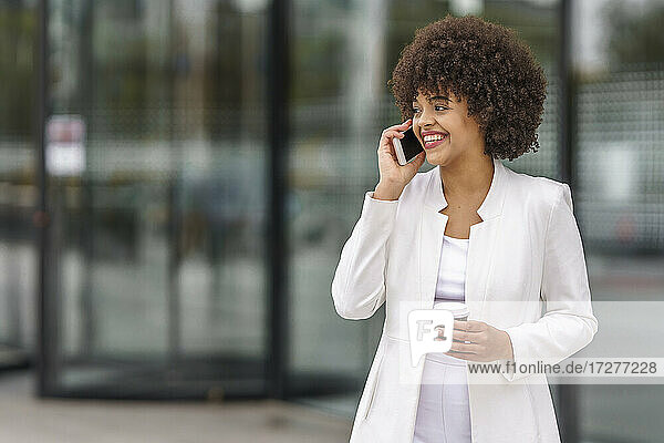 Geschäftsfrau mit Kaffeetasse  die im Freien stehend mit ihrem Mobiltelefon spricht