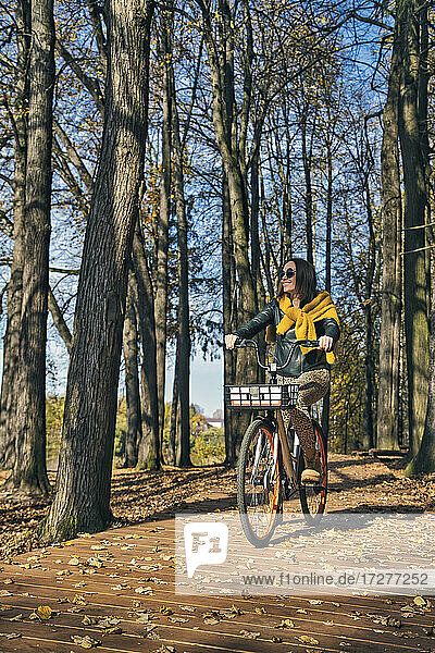 Glückliche Frau schaut weg  während sie an einem sonnigen Tag im Park Fahrrad fährt