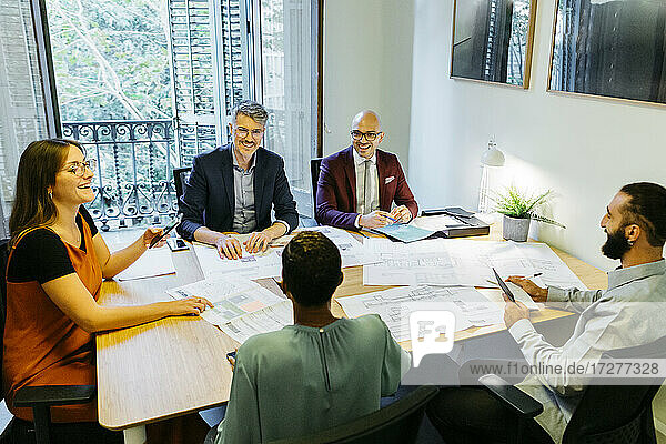 High angle view of businessmen and businesswomen discussing over blueprint on table in office
