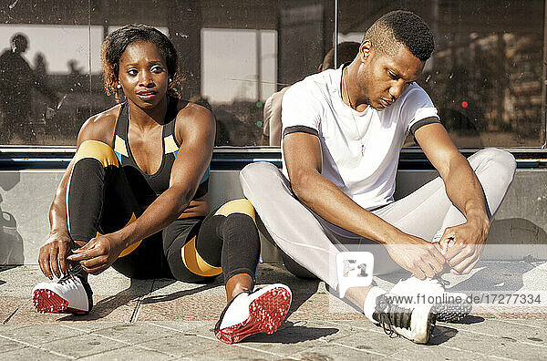 Sportler binden sich die Schnürsenkel  während sie auf dem Bürgersteig der Stadt sitzen