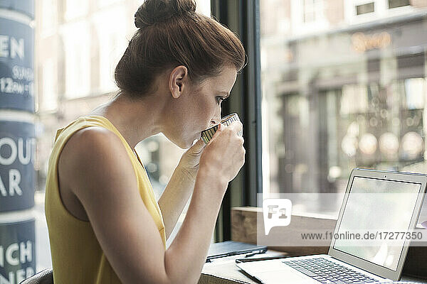 Junge Frau trinkt Kaffee und benutzt einen Laptop in einem Cafe