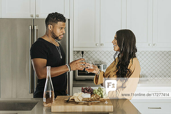 Ehepaar stößt mit einem Weinglas an  während sie in der Küche zu Hause stehen