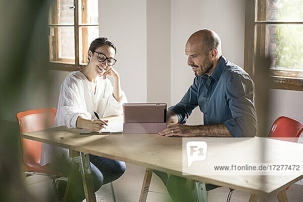 Geschäftsfrau  die in einen Notizblock schreibt und neben einem Mann sitzt  der ein digitales Tablet im Büro benutzt