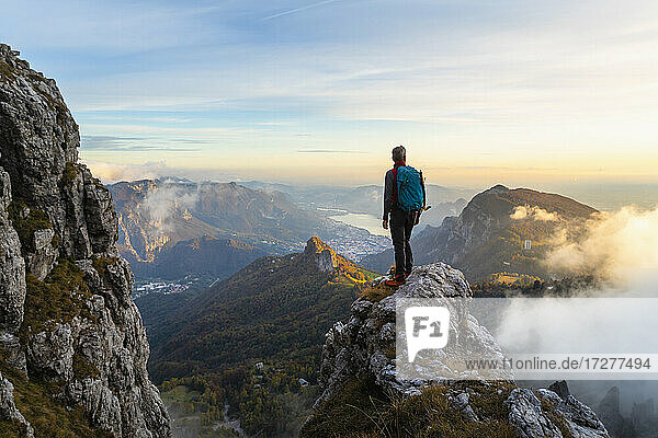 Pensive hiker looking at view while standing on mountain peak during sunrise at Bergamasque Alps  Italy