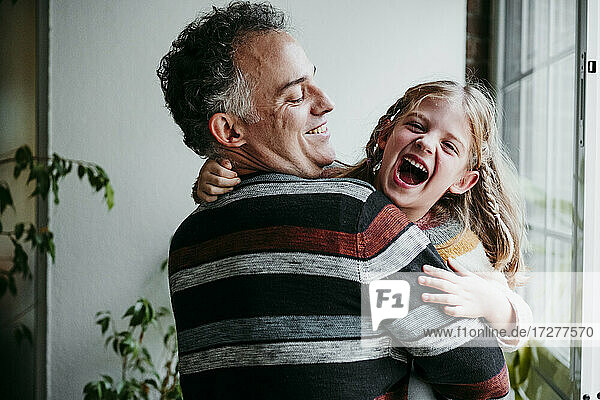Lächelnder Vater mit verspielter Tochter am Fenster stehend zu Hause