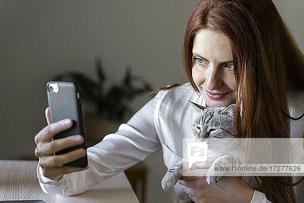 Young woman taking smartphone selfie with cat on lap