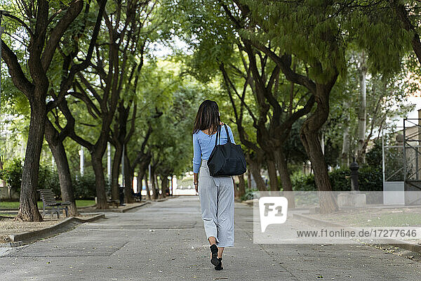 Rückansicht einer Frau mit Handtasche auf dem Fußweg im Park