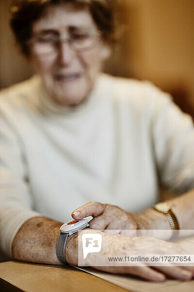 Runzlige  besorgte Frau drückt Notrufknopf am Handgelenk über Tisch zu Hause