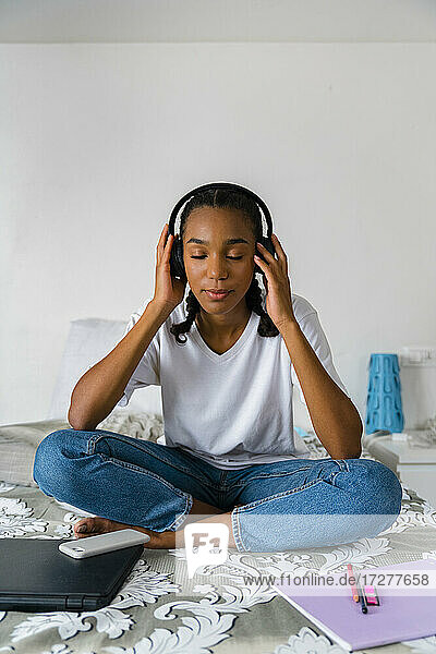 Teenager-Mädchen mit gekreuzten Beinen beim Musikhören  während sie zu Hause sitzt