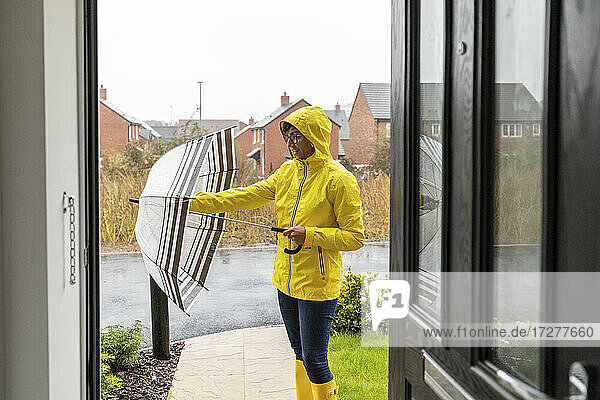 Mittlere erwachsene Frau  die ihren Regenschirm schließt  bevor sie nach Hause geht