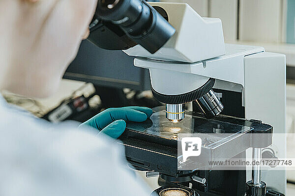 Junge Frau  die einen Objektträger mit menschlichem Gehirn unter dem Mikroskop analysiert  während sie im Labor sitzt