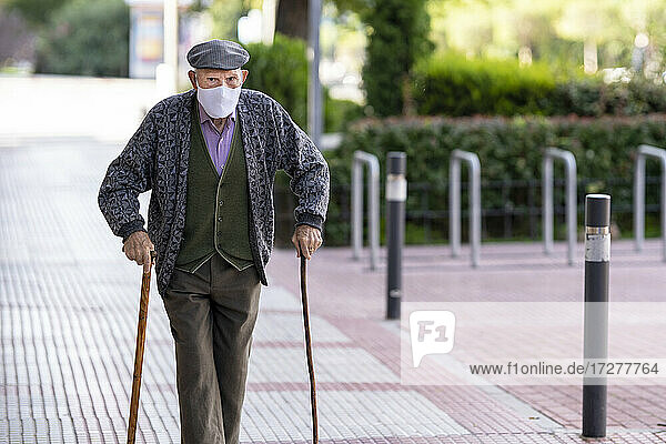 Senior man wearing protective face mask walking on footpath during COVID-19