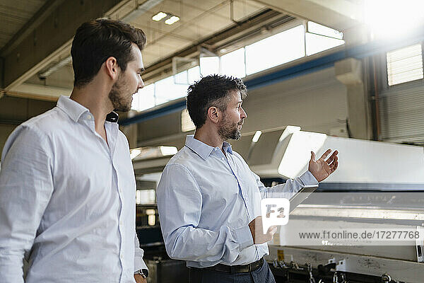 Reifer Geschäftsmann mit digitalem Tablet im Gespräch mit einem Kollegen  während er in einer Fabrik steht