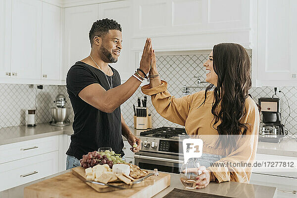Lächelnder Mann und lächelnde Frau  die sich in der Küche zu Hause die Hand reichen