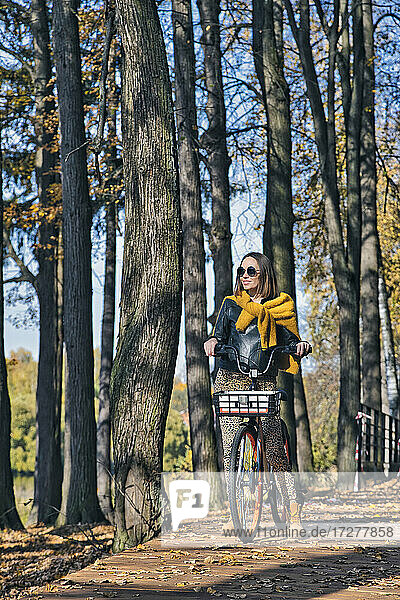 Frau fährt Fahrrad und schaut in einem öffentlichen Park an einem sonnigen Tag weg