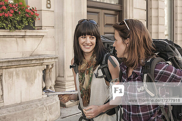 Smiling woman talking with female friend while walking in city