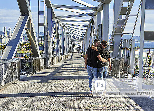 Homosexual couple kissing while walking on bridge during sunny day