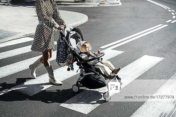 Mutter mit kleinem Jungen im Kinderwagen beim Überqueren der Straße in der Stadt an einem sonnigen Tag