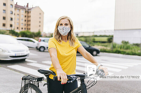 Frau mit Gesichtsschutzmaske steht mit Fahrrad auf der Straße in der Stadt