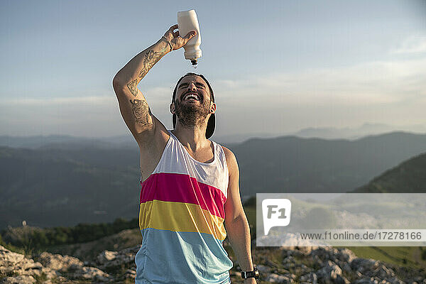 Sportler  der sich Wasser ins Gesicht gießt  während er auf einem Berg gegen den klaren Himmel steht