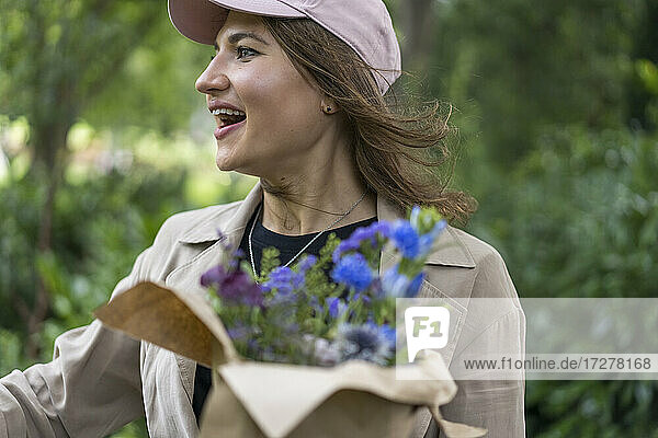 Junge Frau schaut mit offenem Mund weg und hält einen Blumenstrauß  während sie im Park steht
