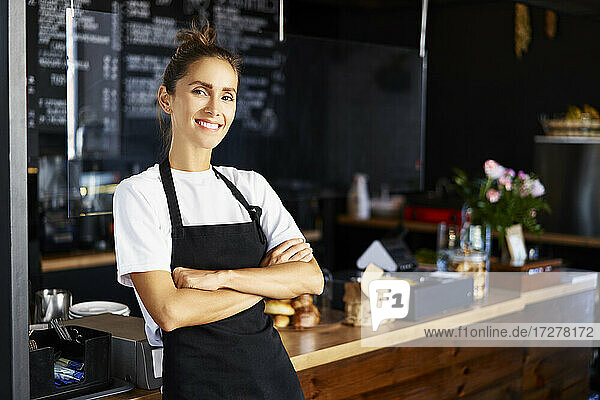 Portrait of smiling barista with arms crossed working at cafe