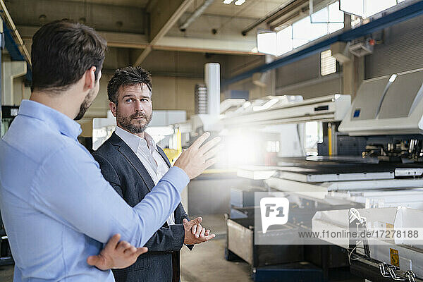 Businessmen discussing with colleague while standing at modern factory