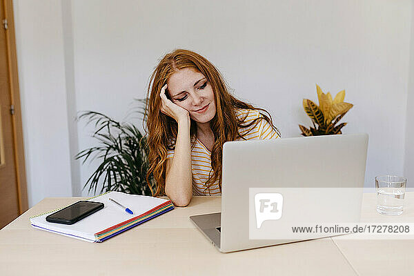 Junge Frau mit Hand in den Haaren  die einen Laptop benutzt  während sie zu Hause sitzt