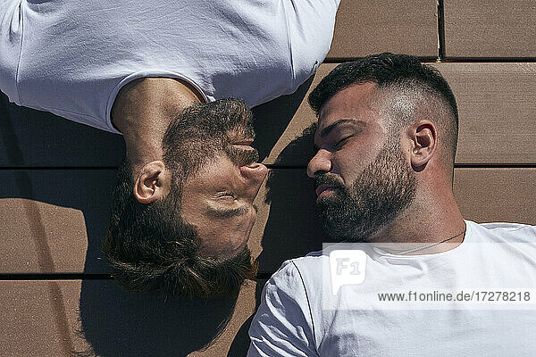Homosexuelles Paar  das an einem sonnigen Tag von Angesicht zu Angesicht auf der Diele liegt