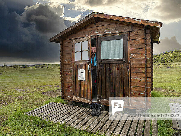 Lächelnder männlicher Tourist  der aus der Tür eines Holzhauses blickt