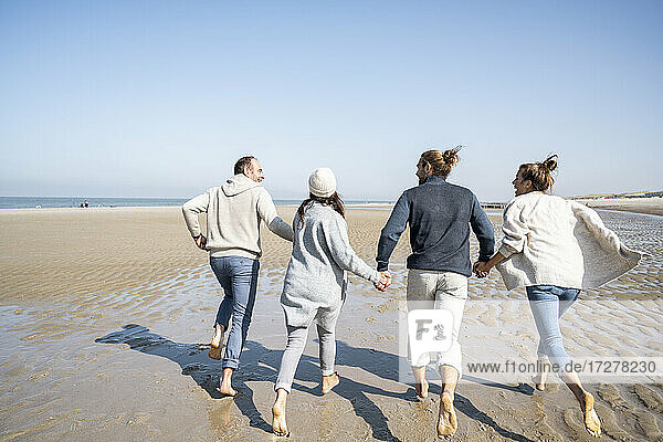 Family holding hands while running on beach