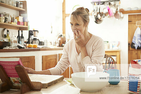 Ältere Frau  die in der Küche sitzend ein Rezeptbuch liest