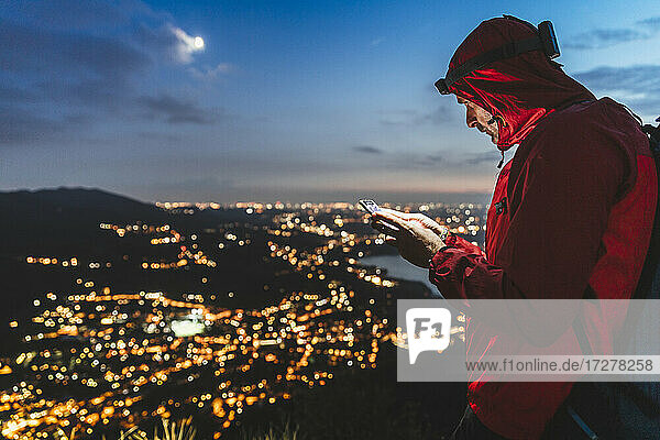 Männlicher Wanderer mit Smartphone und beleuchteter Stadt am Nachthimmel