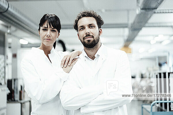 Selbstbewusste Wissenschaftlerin mit Hand auf der Schulter eines männlichen Kollegen in einem hellen Labor