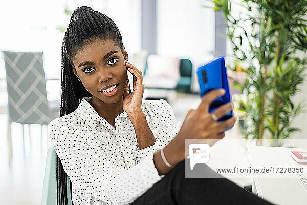 Junge Unternehmerin  die ein Selfie mit ihrem Smartphone macht  während sie zu Hause sitzt