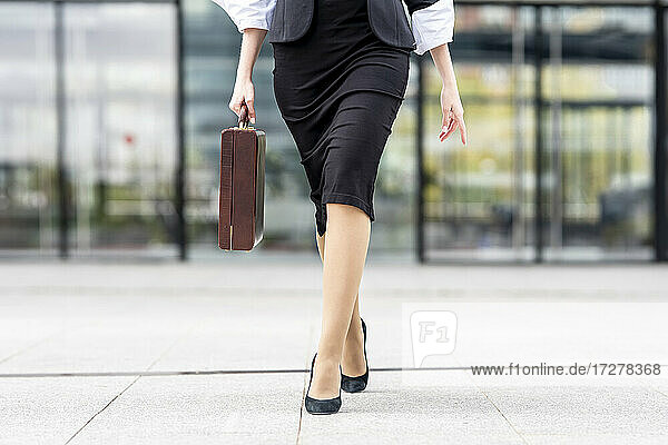 Junge Geschäftsfrau mit hohen Absätzen und Aktentasche auf dem Fußweg