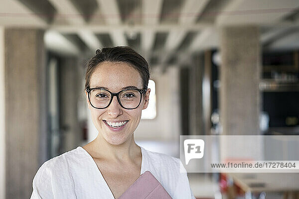 Smiling businesswoman wearing eyeglasses holding digital tablet while standing at office