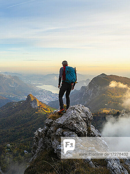 Pensive hiker with backpack standing on mountain peak during sunrise at Bergamasque Alps  Italy