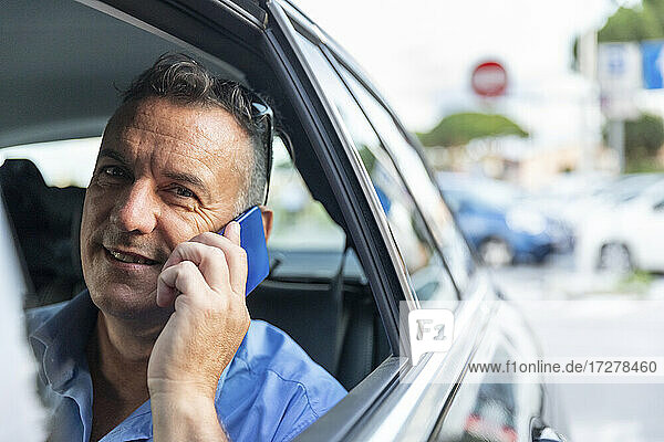 Lächelnder männlicher Berufstätiger  der im Auto sitzend über sein Handy spricht