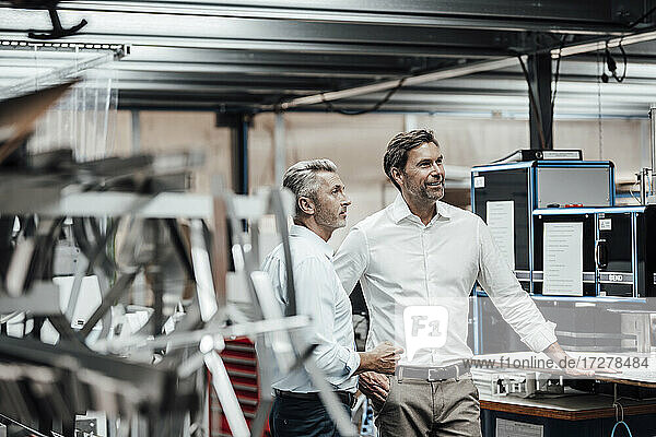 Mature colleague discussing with smiling manager while standing by manufacturing machinery in factory