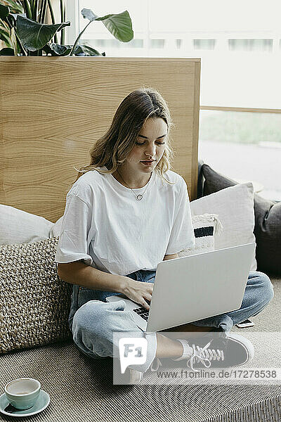 Konzentrierte Frau mit Laptop auf dem Sofa sitzend