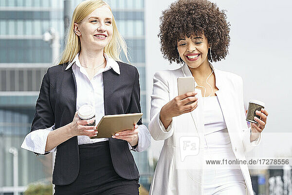 Smiling businesswoman using mobile phone while walking with colleague outdoors
