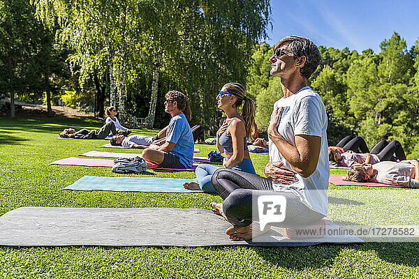 Ältere männliche und weibliche Touristen üben Yoga auf einer Matte in einem Gesundheitszentrum an einem sonnigen Tag