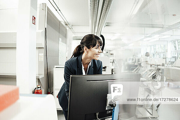 Smiling businesswoman looking away while standing in front of computer monitor at industry