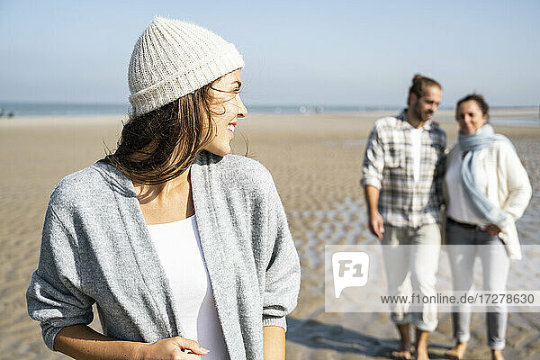Young woman looking over shoulder to man and mother walking in background at beach