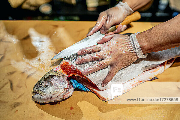 Männlicher Koch schneidet Fisch am Tresen eines Restaurants
