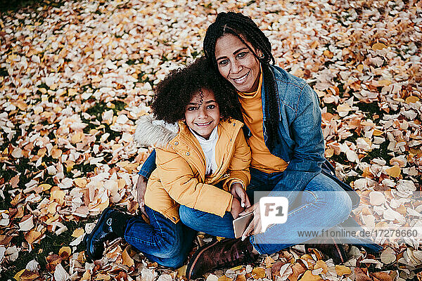 Mutter und Tochter sitzen lächelnd auf gefallenen Blättern im Park